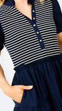 A close-up of a woman wearing a navy blue and cream striped short-sleeve top with a buttoned collar and a navy blue tiered skirt with side pockets.