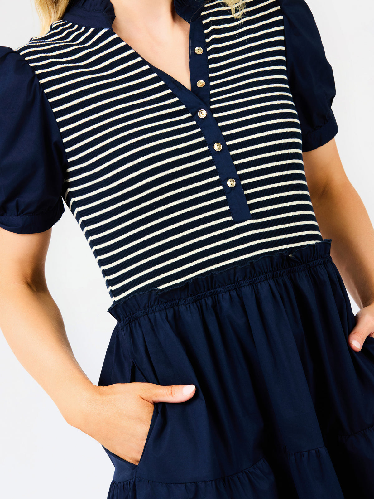 A close-up of a woman wearing a navy blue and cream striped short-sleeve top with a buttoned collar and a navy blue tiered skirt with side pockets.