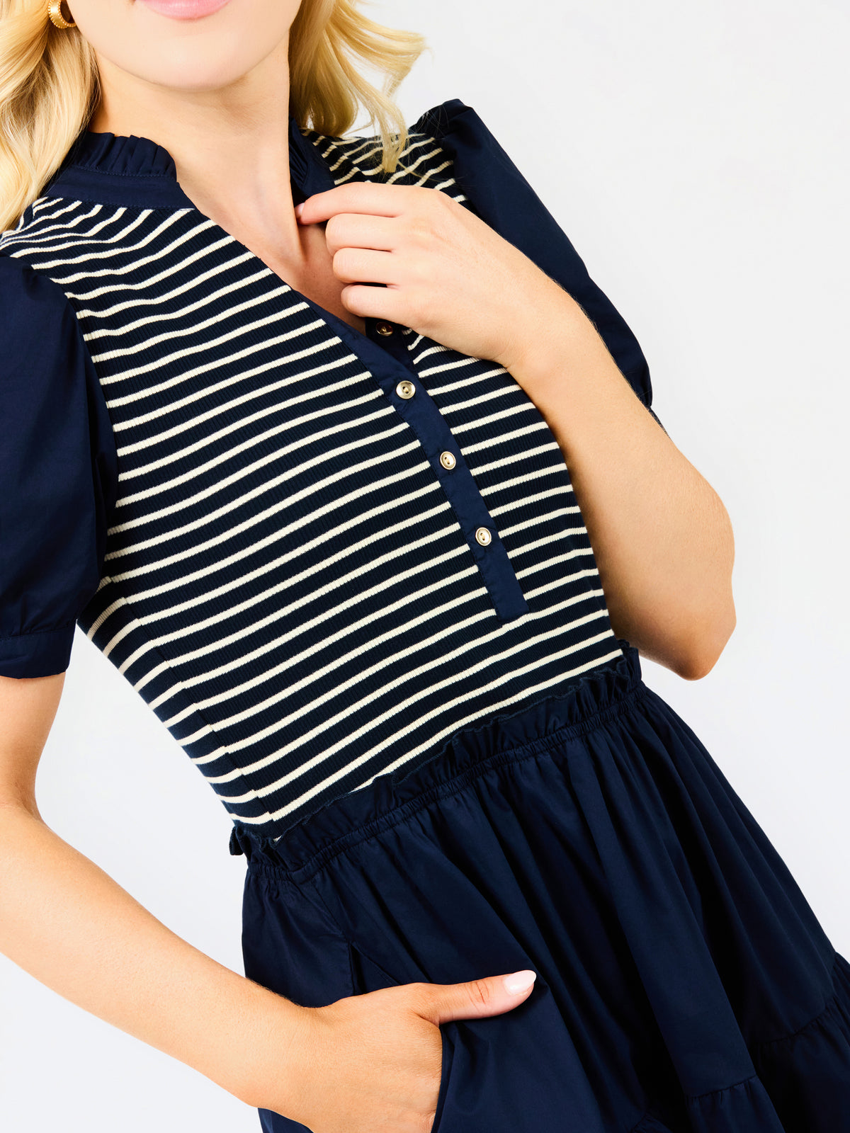 A close-up of a woman wearing a navy blue and white horizontally striped short-sleeve top with a buttoned henley-style neckline and a navy skirt, against a plain white background.