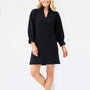 A woman modeling a black long-sleeve mini dress with a V-neckline and cuffed sleeves, paired with white sneakers, against a plain white studio background.