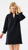 A blonde woman modeling a black long-sleeve mini dress with a V-neck and gathered cuffs, photographed against a clean white studio background.