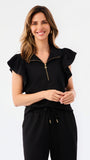 A woman modeling a black two-piece outfit consisting of a short-sleeve top with ruffled shoulders and a gold zipper, paired with matching wide-leg pants, against a plain white studio background.