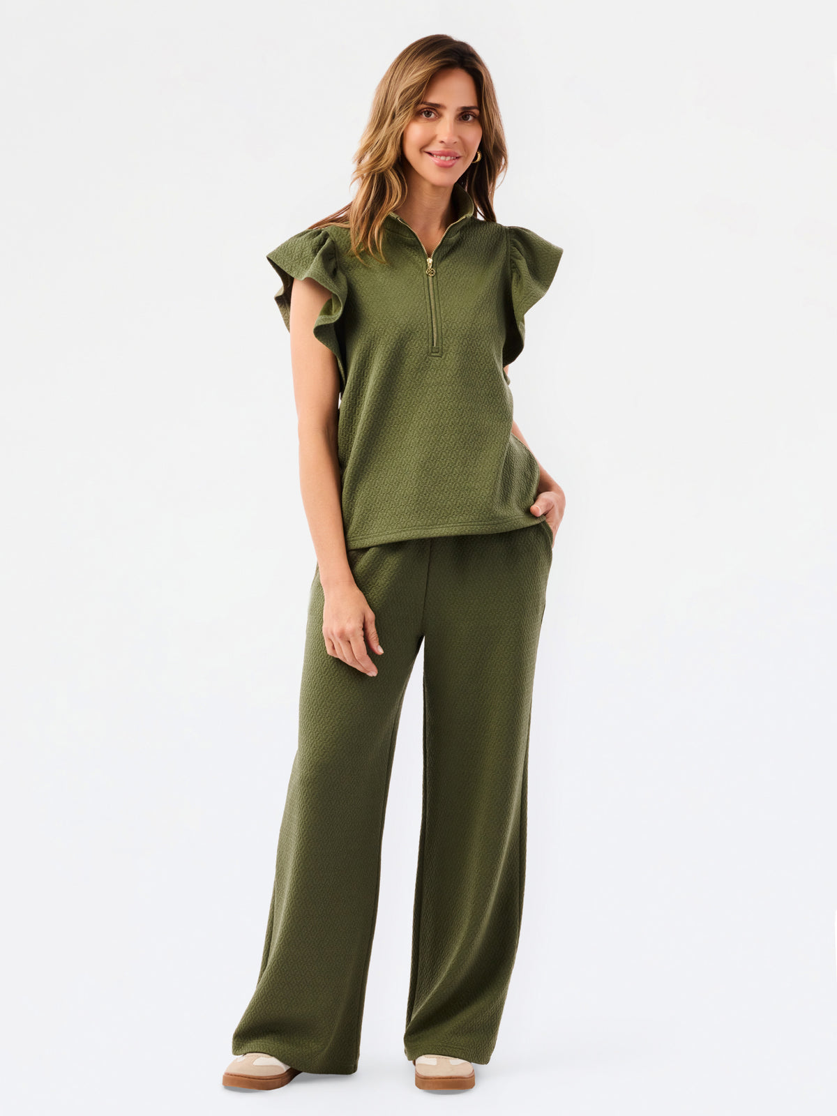 A woman modeling a matching olive green two-piece set consisting of a ruffled short-sleeve quarter-zip top and wide-leg pants, photographed against a clean white studio background.
