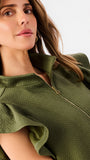 A woman modeling a matching olive green two-piece set consisting of a ruffled short-sleeve quarter-zip top and wide-leg pants, photographed against a clean white studio 