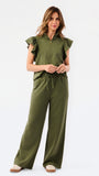 A woman modeling a matching olive green two-piece set consisting of a ruffled short-sleeve quarter-zip top and wide-leg pants, photographed against a clean white studio 