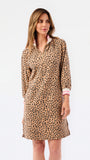 A woman modeling a leopard print long-sleeve shirt dress with a pink inner collar and cuffs, set against a plain white studio background.