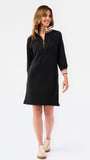 A woman modeling a black long-sleeve shift dress with a half-zip neckline and striped trim details on the collar and cuffs, set against a plain white studio background.