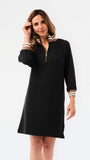 A woman modeling a black long-sleeve shift dress with a half-zip neckline and striped trim details on the collar and cuffs, set against a plain white studio background.