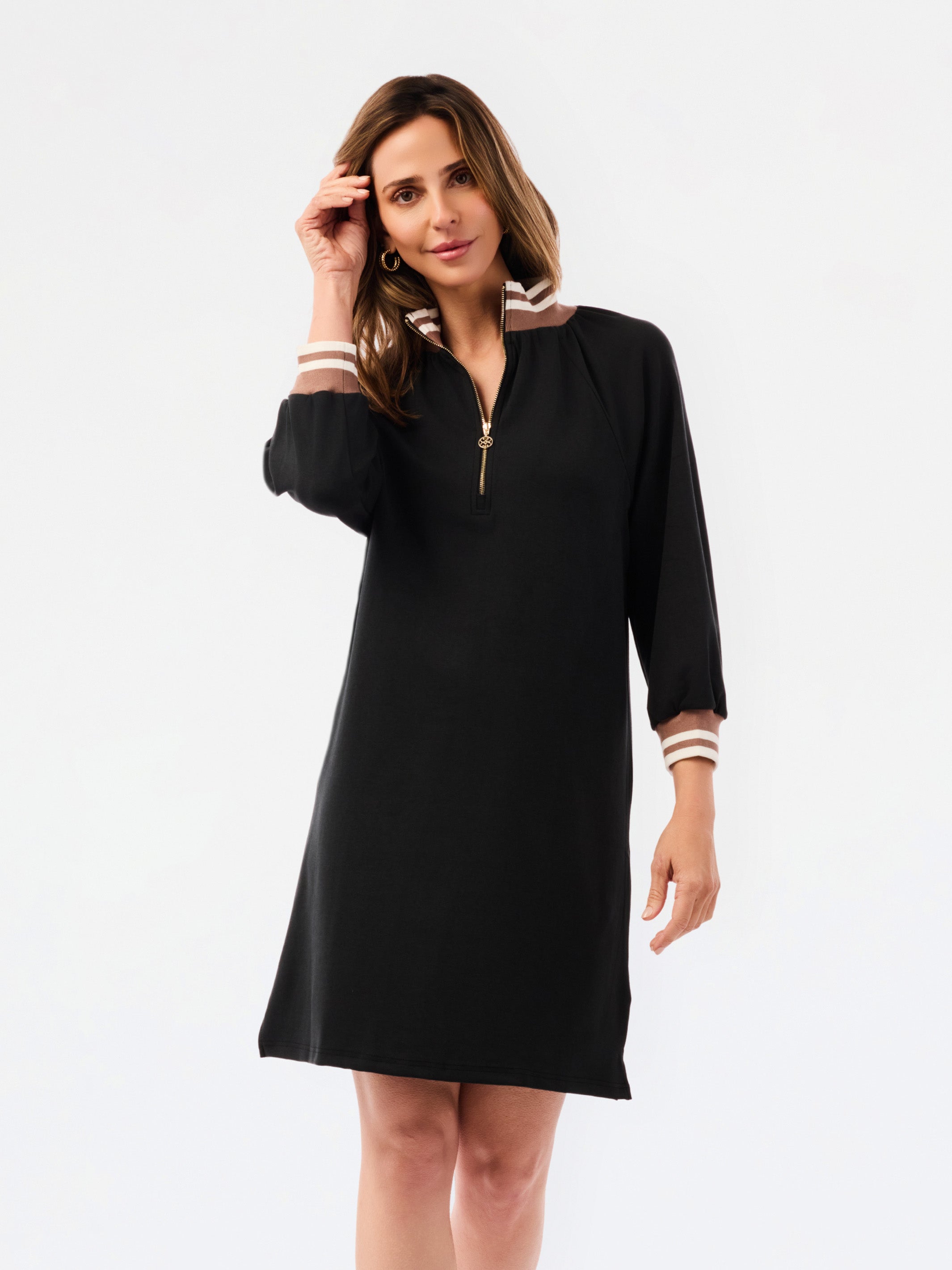 A woman modeling a black long-sleeve shift dress with a half-zip neckline and striped trim details on the collar and cuffs, set against a plain white studio background.