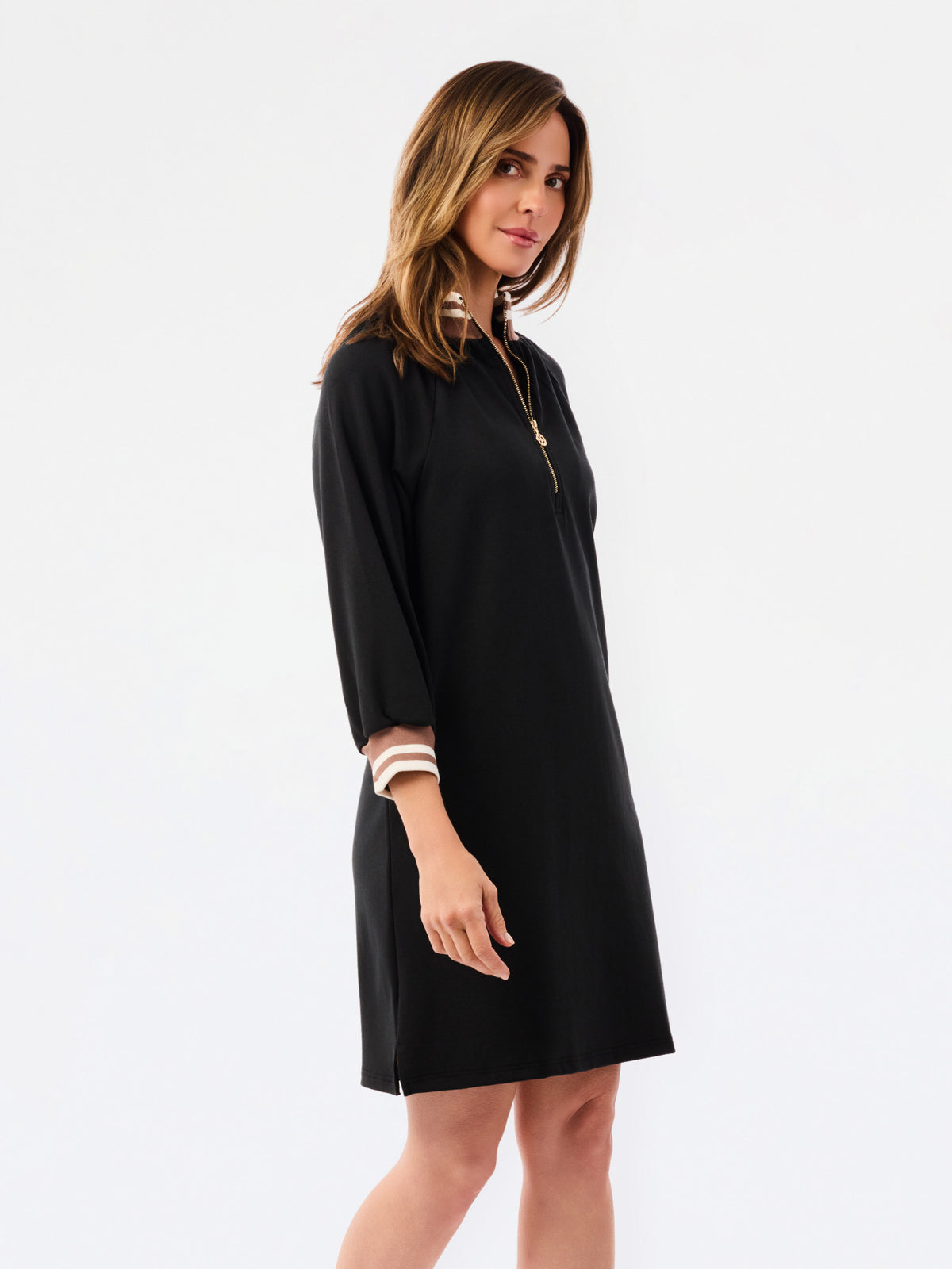 A woman modeling a black long-sleeve shift dress with a half-zip neckline and striped trim details on the collar and cuffs, set against a plain white studio background.