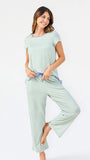 Woman wearing a green and white striped short sleeve pajama set with blue trim on a white background