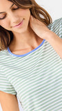 Woman wearing a green and white striped short sleeve pajama set with blue trim on a white background