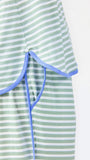 Woman wearing a green and white striped short sleeve pajama set with blue trim on a white background