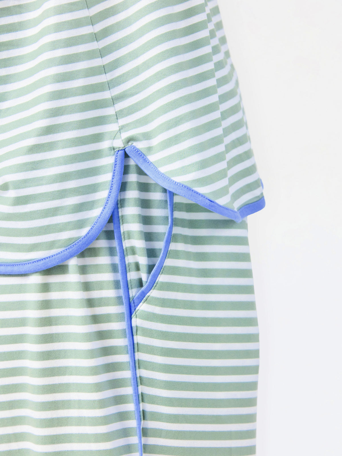 Woman wearing a green and white striped short sleeve pajama set with blue trim on a white background