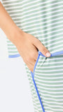 Woman wearing a green and white striped short sleeve pajama set with blue trim on a white background