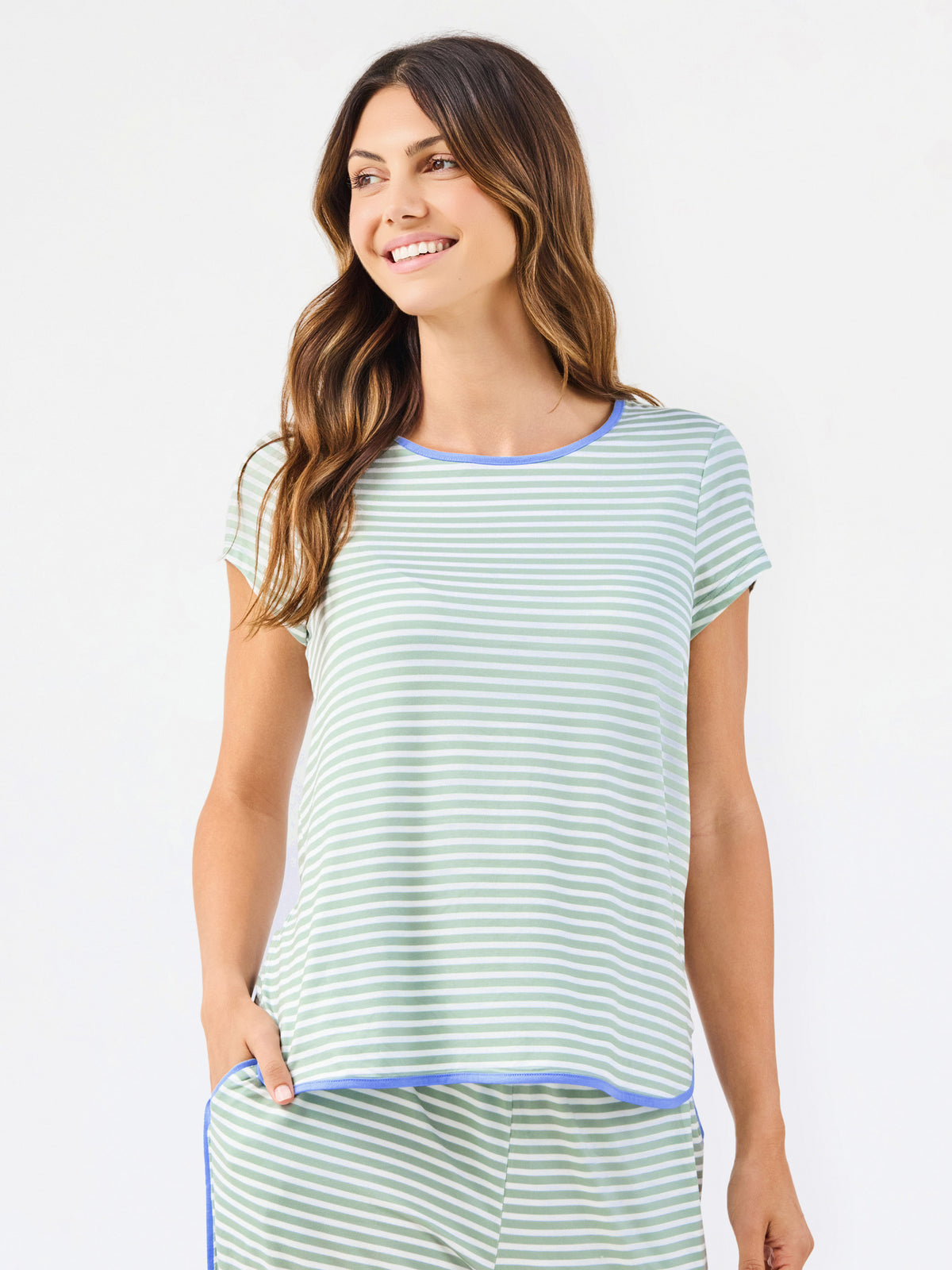 Woman wearing a green and white striped short sleeve pajama set with blue trim on a white background