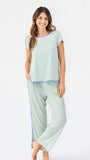 Woman wearing a green and white striped short sleeve pajama set with blue trim on a white background