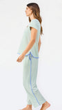 Woman wearing a green and white striped short sleeve pajama set with blue trim on a white background