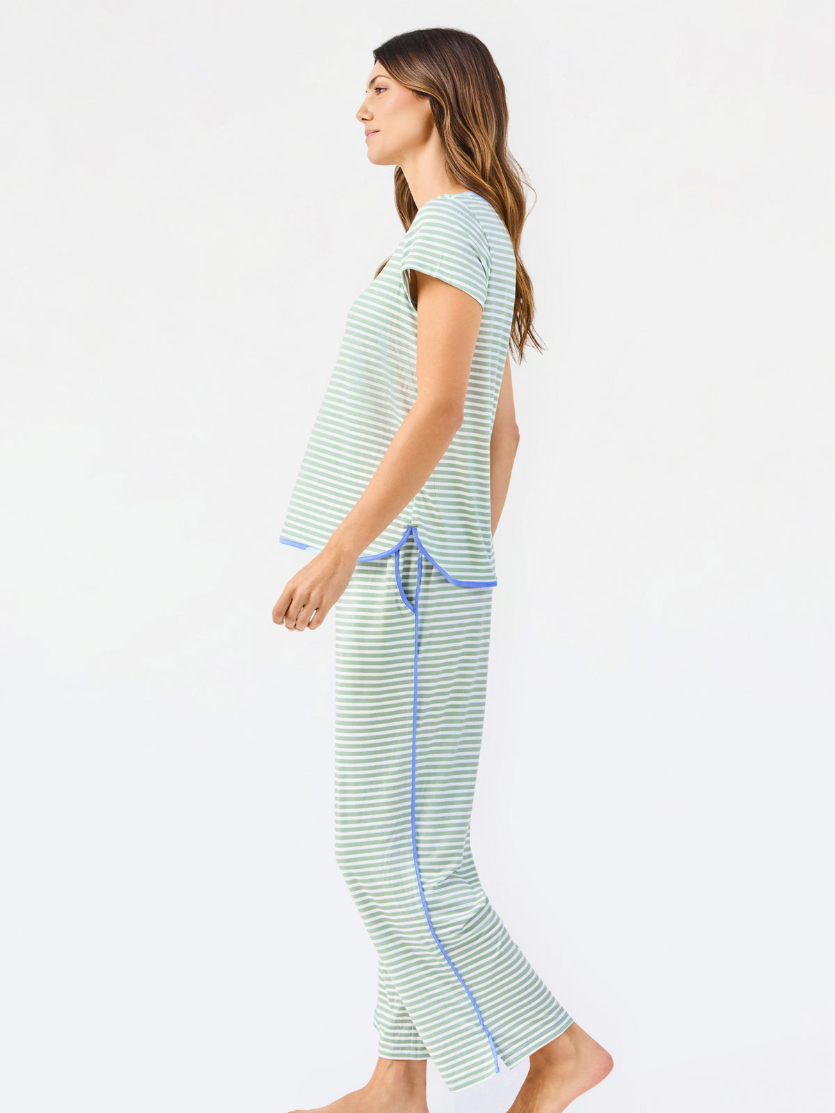 Woman wearing a green and white striped short sleeve pajama set with blue trim on a white background