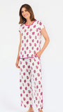 Brown haired woman wearing a  pink and green floral pajama set with pink trim on a white background