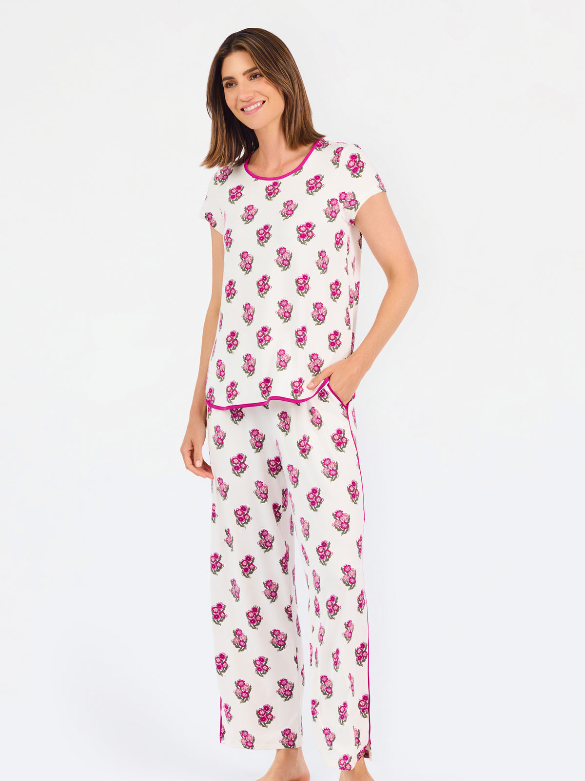 Brown haired woman wearing a  pink and green floral pajama set with pink trim on a white background