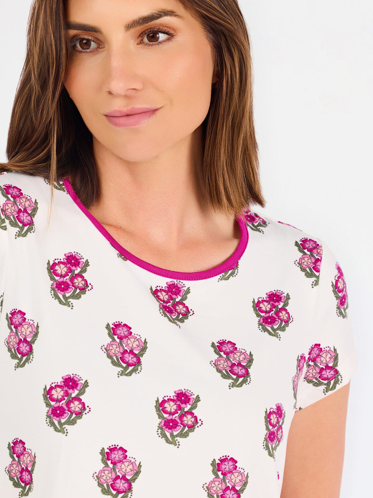 Brown haired woman wearing a  pink and green floral pajama set with pink trim on a white background
