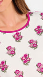 Brown haired woman wearing a  pink and green floral pajama set with pink trim on a white background