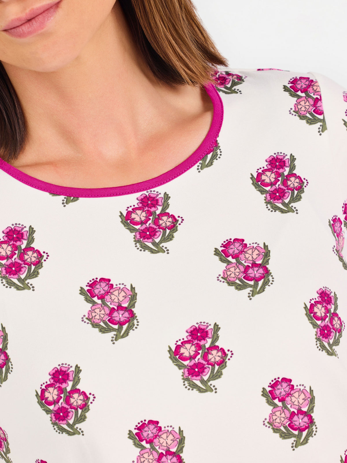 Brown haired woman wearing a  pink and green floral pajama set with pink trim on a white background