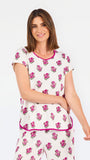 Brown haired woman wearing a  pink and green floral pajama set with pink trim on a white background