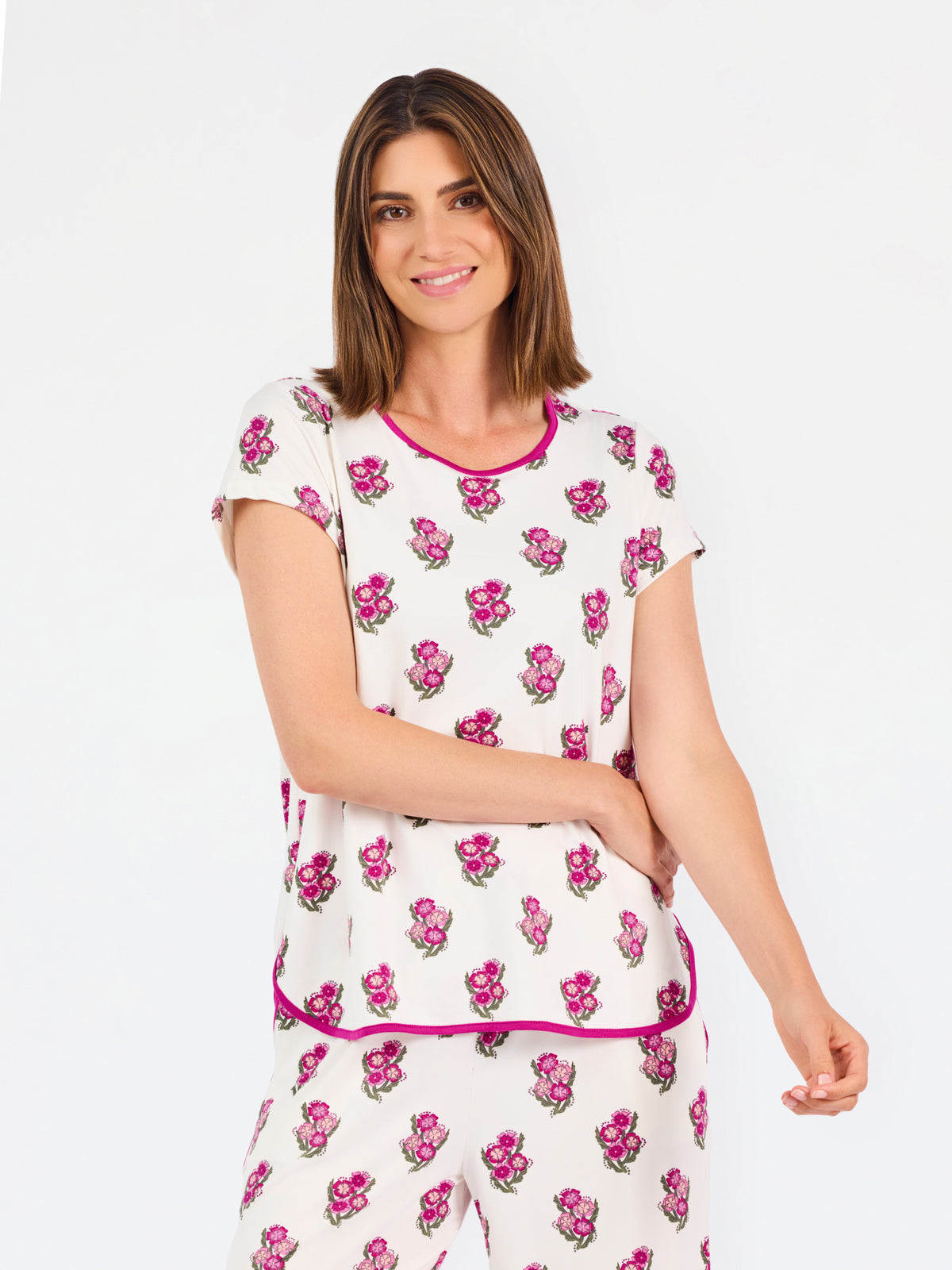 Brown haired woman wearing a  pink and green floral pajama set with pink trim on a white background