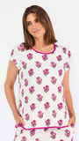 Brown haired woman wearing a  pink and green floral pajama set with pink trim on a white background