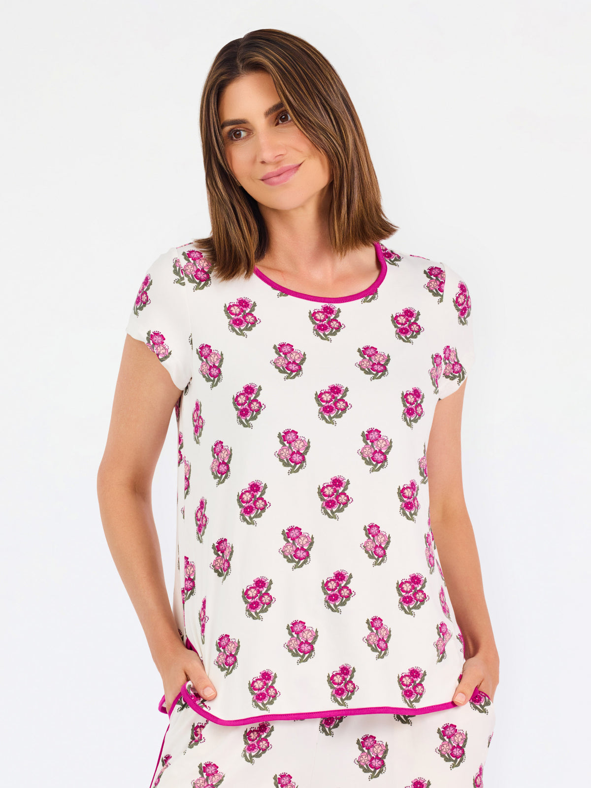 Brown haired woman wearing a  pink and green floral pajama set with pink trim on a white background