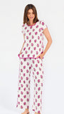 Brown haired woman wearing a  pink and green floral pajama set with pink trim on a white background