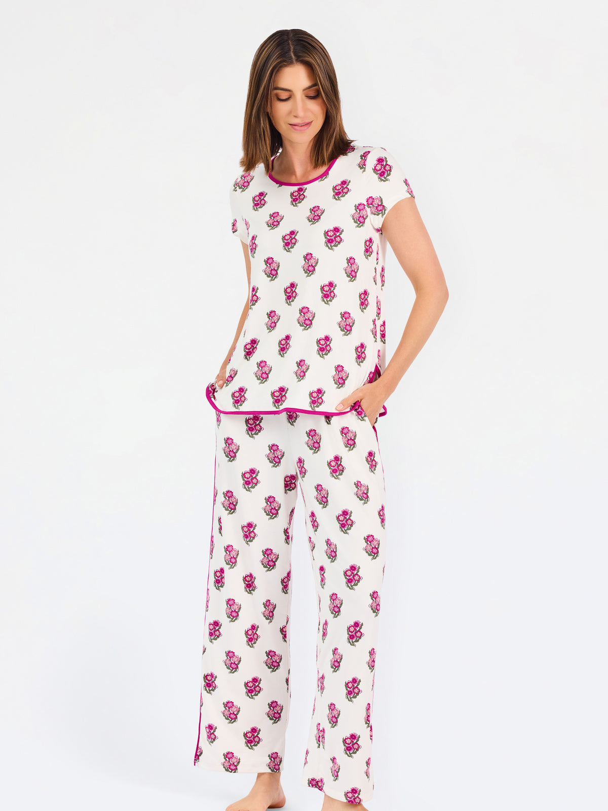 Brown haired woman wearing a  pink and green floral pajama set with pink trim on a white background