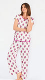 Brown haired woman wearing a  pink and green floral pajama set with pink trim on a white background