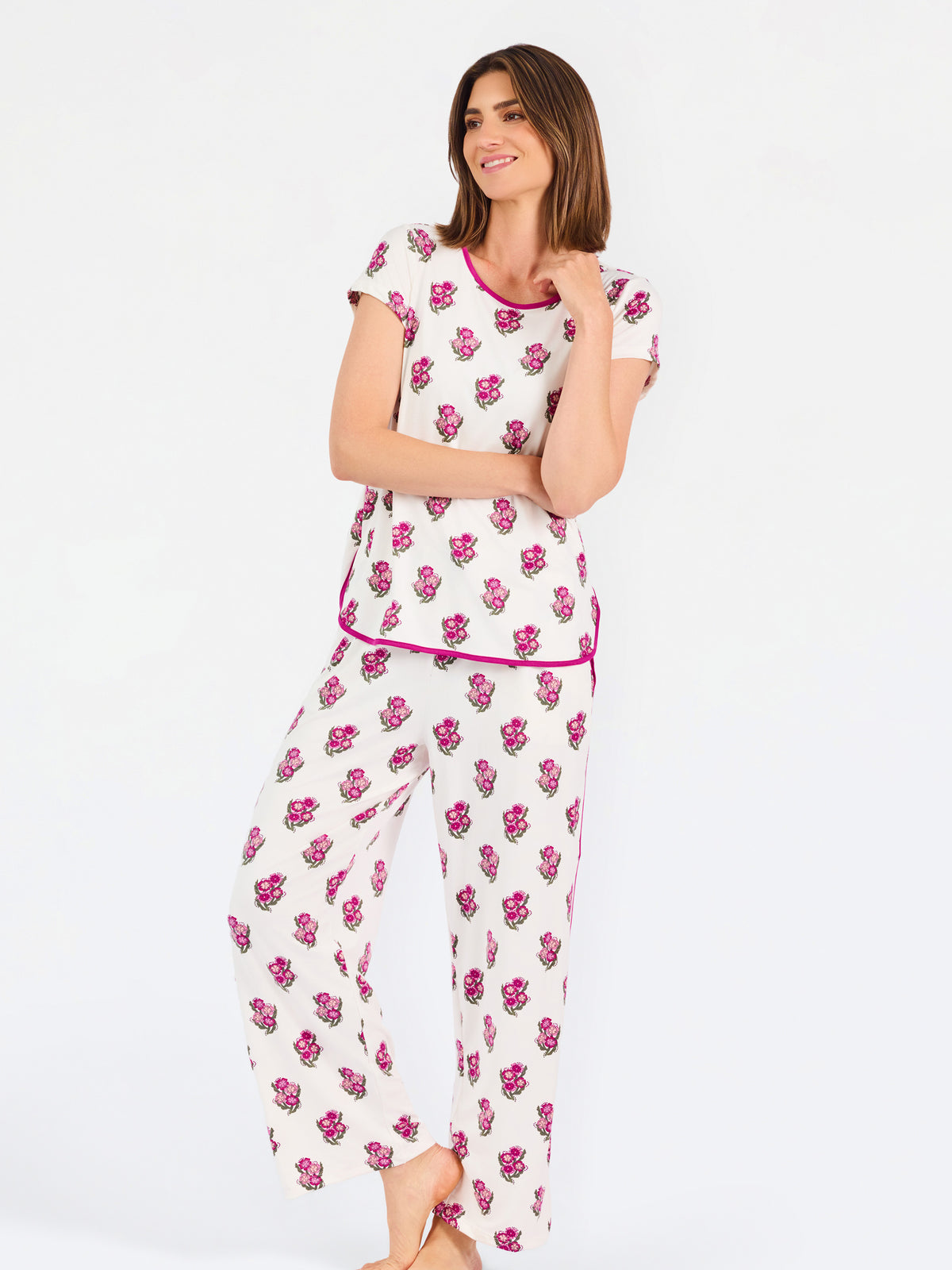 Brown haired woman wearing a  pink and green floral pajama set with pink trim on a white background