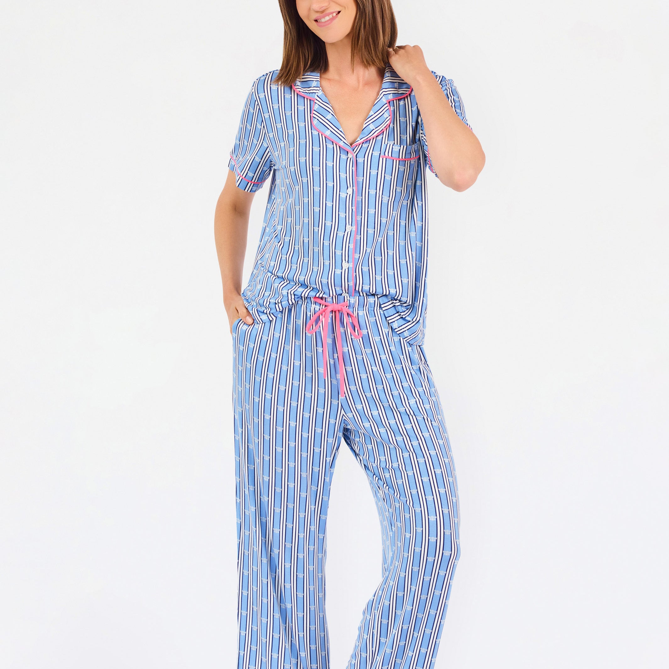 Woman wearing a blue striped pajama set with bees and stripes and a pink trim on a white background