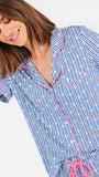 Woman wearing a blue striped pajama set with bees and stripes and a pink trim on a white background