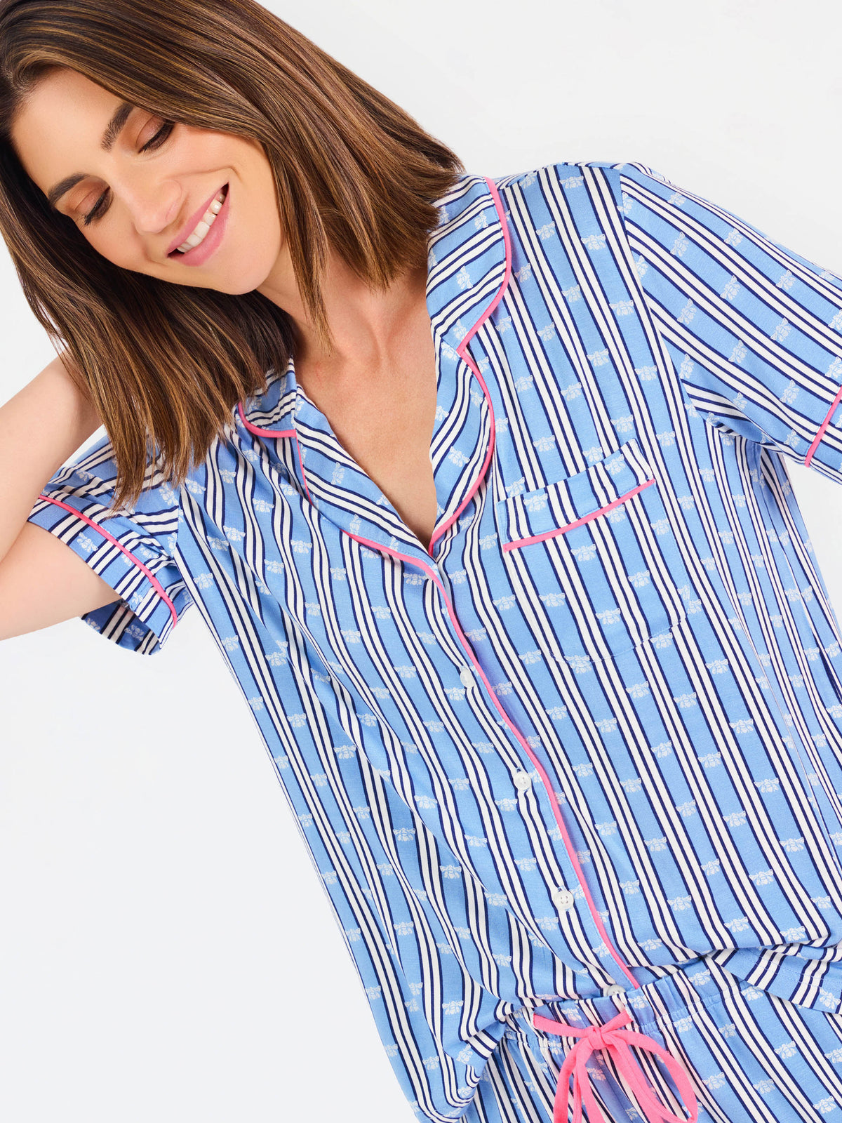 Woman wearing a blue striped pajama set with bees and stripes and a pink trim on a white background