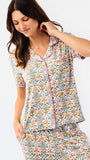 A woman modeling a two-piece pajama set with a colorful geometric pattern, featuring a short-sleeve button-up top and matching pants, set against a plain white background.