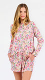Blonde long haired woman wearing a multi colored floral long sleeve and shorts pajama set on a white background