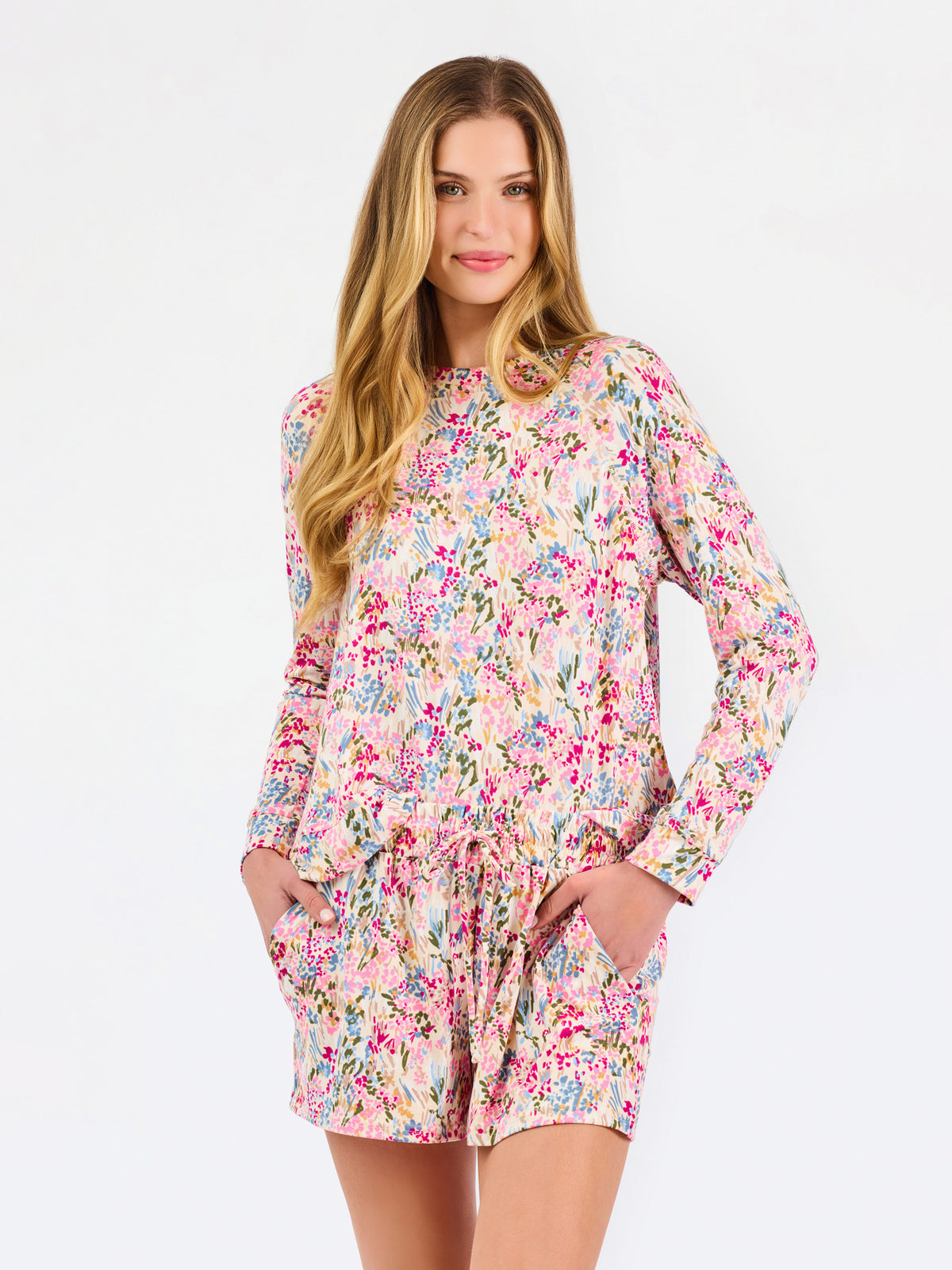Blonde long haired woman wearing a multi colored floral long sleeve and shorts pajama set on a white background
