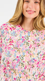 Blonde long haired woman wearing a multi colored floral long sleeve and shorts pajama set on a white background