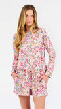 Blonde long haired woman wearing a multi colored floral long sleeve and shorts pajama set on a white background