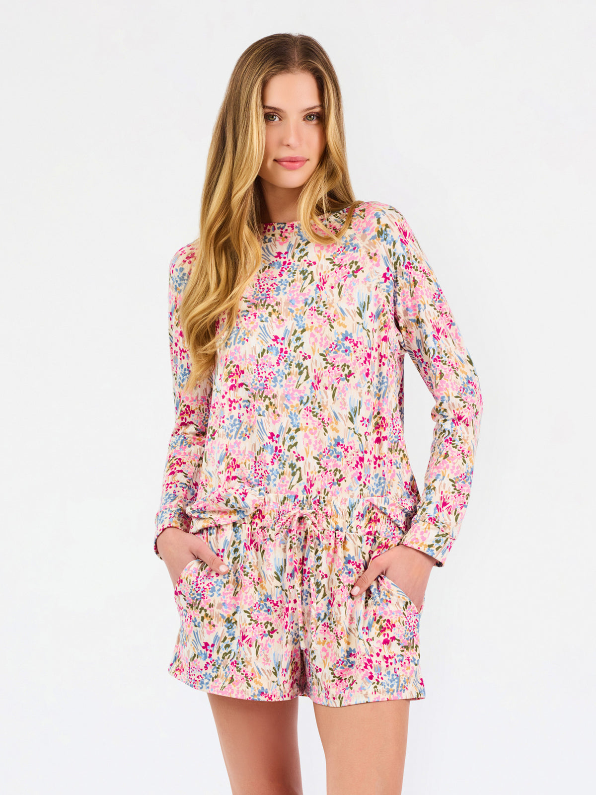 Blonde long haired woman wearing a multi colored floral long sleeve and shorts pajama set on a white background