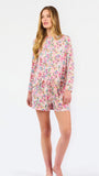 Blonde long haired woman wearing a multi colored floral long sleeve and shorts pajama set on a white background