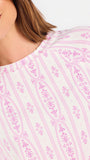 Short brown haired woman wearing a pink/purple floral pajama set on a white background