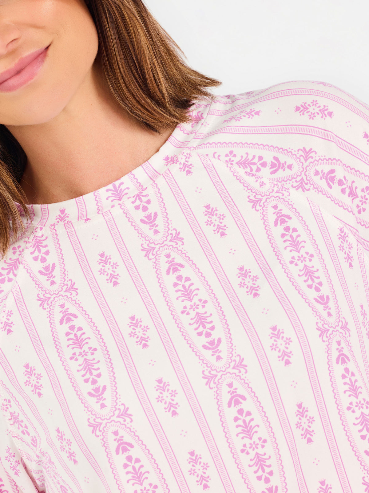 Short brown haired woman wearing a pink/purple floral pajama set on a white background