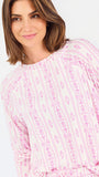 Short brown haired woman wearing a pink/purple floral pajama set on a white background