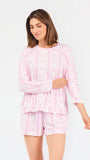 Short brown haired woman wearing a pink/purple floral pajama set on a white background